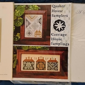 May include: Three cross-stitch sampler patterns are displayed. The first features a house and text, "A Shaker Sampler." The second, "Quaker House Samplers," shows framed samplers. The third, "A Sampler for My Mother," has a floral design. All are in protective sleeves.