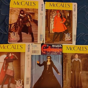 May include: Five sewing pattern envelopes for costumes. Top left: McCall's M7646 with a hooded dark outfit. Top right: McCall's M7989 with an orange coat. Bottom left: McCall's M7645 with a red cape. Center: Simplicity 5380 with a black coat. Bottom right: McCall's M7856 with a long dark robe.