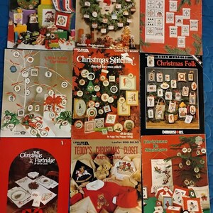 May include: A collection of nine vintage cross stitch pattern books with Christmas themes. The books feature a variety of designs, including ornaments, wreaths, and holiday characters. The covers are colorful and feature illustrations of the patterns.