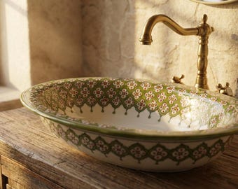 May include: Oval ceramic bathroom sink with a decorative green and red floral pattern. The sink is set on a wooden cabinet and features a brass faucet. The design is reminiscent of vintage or farmhouse styles.