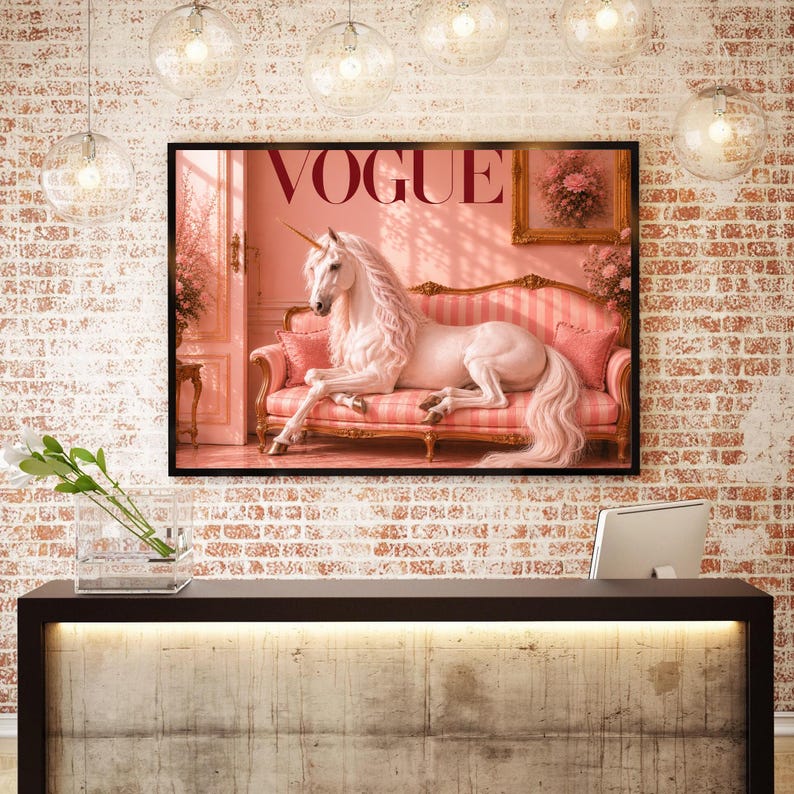 May include: A framed print featuring the word "VOGUE" in a serif font, with a pink background. The image depicts a white unicorn reclining on a pink striped sofa. The artwork is displayed on a brick wall.