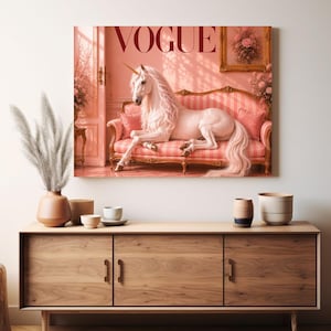 May include: A framed canvas print featuring a unicorn lounging on a pink striped sofa. The word "VOGUE" is displayed at the top. The artwork is set in a pink-toned room with floral accents and a gold-framed picture.