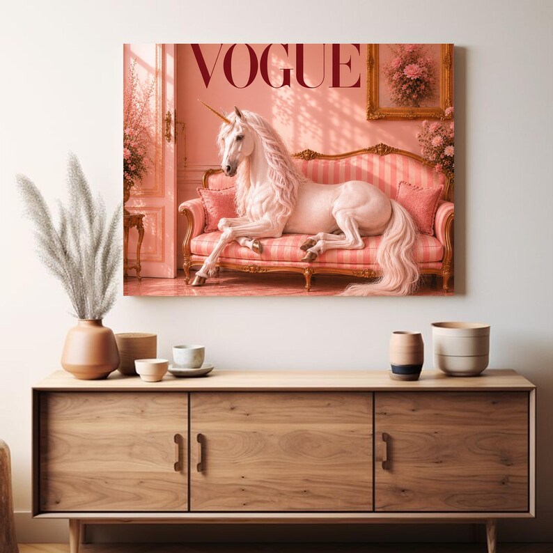 May include: A framed canvas print featuring a unicorn lounging on a pink striped sofa. The word "VOGUE" is displayed at the top. The artwork is set in a pink-toned room with floral accents and a gold-framed picture.