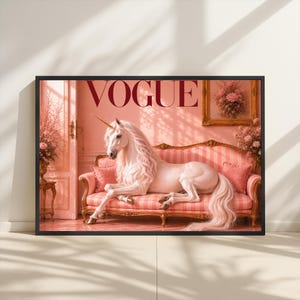 May include: A framed print featuring a white unicorn with a golden horn, reclining on a pink striped sofa. The word "VOGUE" is displayed in burgundy above the unicorn. The background is a pink room with floral accents.
