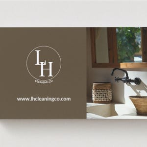 Op de afbeelding: Visitekaartontwerp voor LH Cleaning Co. De kaart heeft een bruine achtergrond met het bedrijfslogo en websiteadres. De rechterkant toont een badkamer met een kraan, wastafel en decoratieve mand.