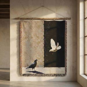 May include: Woven wall hanging featuring a split design with a beige and black background. A black bird stands on a ledge, while a white dove flies in the black section. The tapestry is hung from a wooden rod.