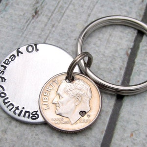 May include: A silver keychain with a round tag that says "counting years 10" and a 2005 dime with a heart on it.