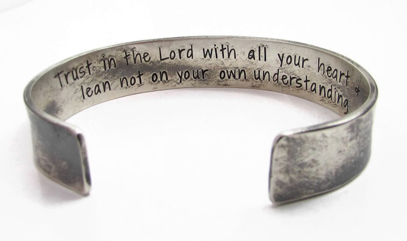 Puede incluir: Pulsera de plata con acabado desgastado y una inscripci&oacute;n grabada: "Trust in the Lord with all your heart lean not on your own understanding."