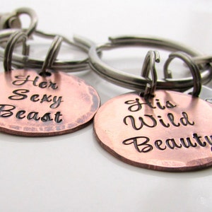 May include: A set of two keychains with metal tags. One tag is copper-colored and reads "Her Sexy Beast", the other is copper-colored and reads "His Wild Beauty". Each keychain has a silver-colored metal ring and clasp.