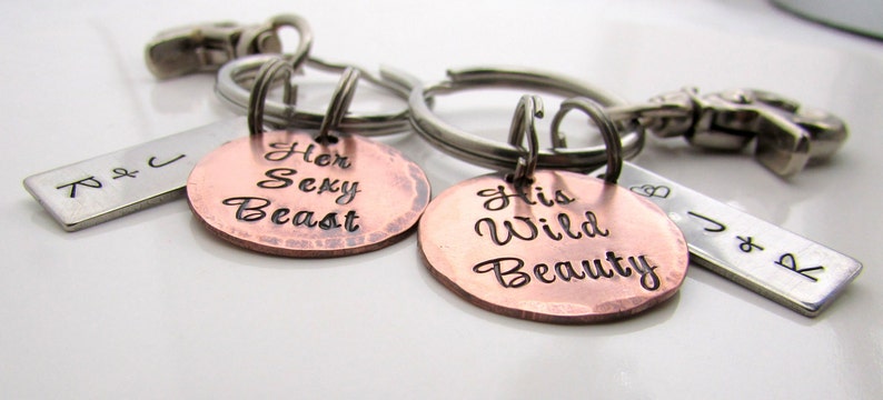 May include: A set of two keychains with metal tags. One tag is copper-colored and reads "Her Sexy Beast", the other is copper-colored and reads "His Wild Beauty". Each keychain has a silver-colored metal ring and clasp.
