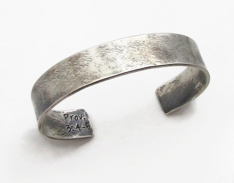 Puede incluir: Pulsera de plata con acabado texturizado y una inscripci&oacute;n que dice "Prov. 3:4-5".