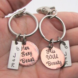 May include: Two keychains with silver rings and lobster claw clasps. Each keychain has a small rectangular tag with initials and a copper-colored circular tag. One reads "Her Sexy Beast," the other "His Wild Beauty."