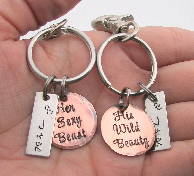 May include: Two keychains with silver rings and lobster claw clasps. Each keychain has a small rectangular tag with initials and a copper-colored circular tag. One reads "Her Sexy Beast," the other "His Wild Beauty."