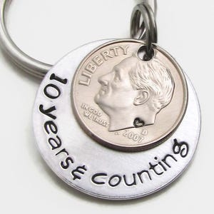 May include: Silver keychain with a silver dime and the text "10 Years Counting" engraved on the front.