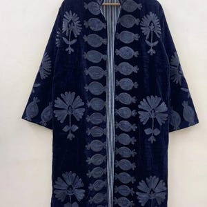 May include: A long, dark navy blue velvet coat featuring intricate tonal embroidery of floral and pomegranate-like motifs. The garment has a high collar, three-quarter length sleeves, and an open front revealing a white and navy blue striped lining.