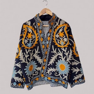 Könnte beinhalten: Marineblaue Jacke mit aufwendiger Blumenstickerei in Gelb, Hellblau und Off-White. Die Jacke hat einen Stehkragen und ist mit einem gestreiften Stoff gefüttert. Das Design umfasst Paisley- und gänseblümchenartige Blumenmuster.