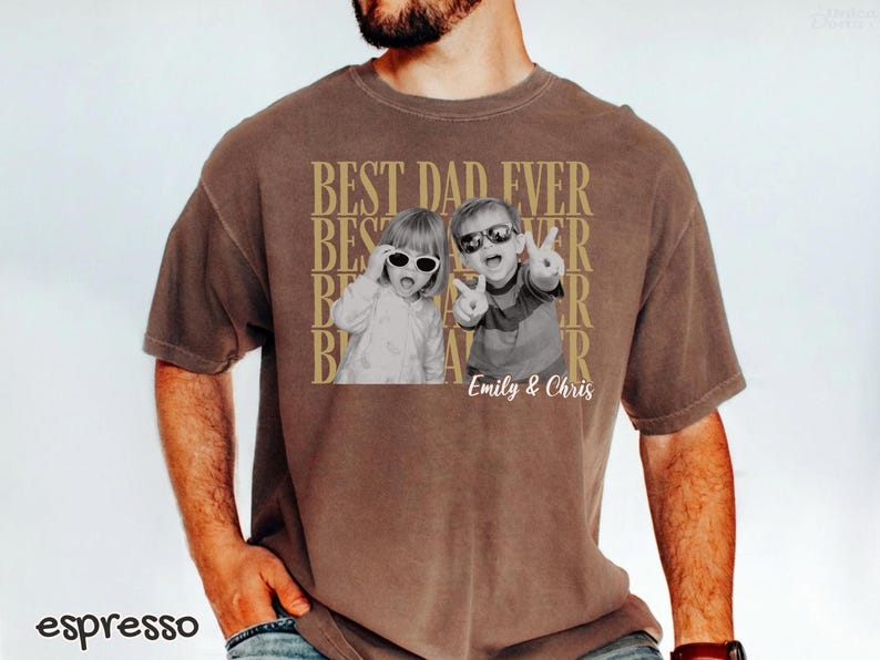 Pu&ograve; includere: T-shirt color espresso con grafica dorata "BEST DAD EVER". Il design include due foto in bianco e nero di bambini con occhiali da sole. I nomi "Emily & Chris" sono stampati sotto le foto.