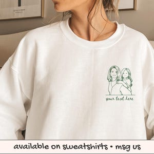 Puede incluir: Sudadera blanca con un dibujo lineal verde de una mujer y un ni&ntilde;o, con el texto "your text here" debajo. La parte inferior de la imagen tiene el texto "available on sweatshirts &bull; msg us".