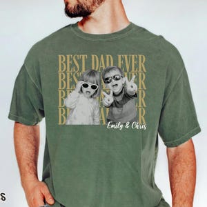 Pu&ograve; includere: T-shirt verde muschio con una foto in bianco e nero di due bambini con occhiali da sole. Le parole "BEST DAD EVER" sono stampate in oro, con i nomi "Emily & Chris" sotto. La maglietta ha una vestibilit&agrave; rilassata.