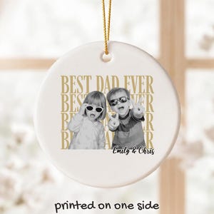 Pu&ograve; includere: Un ornamento natalizio rotondo in ceramica bianca con un cordino dorato per appenderlo. Presenta una foto in bianco e nero di due bambini con occhiali da sole. Il testo "BEST DAD EVER" &egrave; stampato in oro, con i nomi "Emily & Chris".
