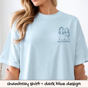 Puede incluir: Camiseta de chambray azul claro con un dise&ntilde;o azul oscuro. La camiseta presenta un dibujo lineal azul oscuro de una mujer y un ni&ntilde;o con el texto "your text here" debajo.