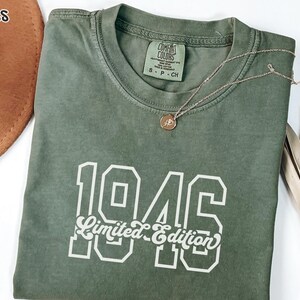 May include: A moss green crew neck t-shirt featuring the white text 1946 Limited Edition in a combination of block and script fonts. The shirt has a Comfort Colors brand label on the inside collar with size S-P-CH visible.