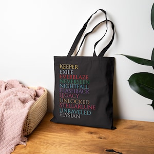 May include: Black tote bag featuring the words "KEEPER, EXILE, EVERBLAZE, NEVERSEEN, NIGHTFALL, FLASHBACK, LEGACY, UNLOCKED, STELLARLUNE, UNRAVELED, ELYSIAN" in various colours. The bag has black handles.