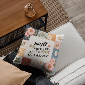 Puede incluir: Cojín decorativo cuadrado con un diseño floral y el texto "MUJER VIRTUOSA ¿QUIÉN LA HALLARÁ?" en escritura negra. El cojín presenta un patrón de patchwork con flores rosas, blancas y amarillas sobre un fondo azul claro.