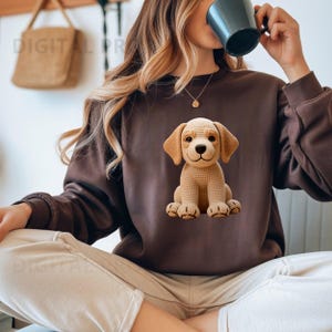 Puede incluir: Una sudadera marrón con un diseño de cachorro tejido. El cachorro es beige y sonríe. La sudadera es de color marrón liso. La imagen también muestra a una persona que lleva la sudadera.