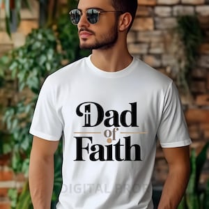 Puede incluir: Camiseta blanca con el texto "Dad of Faith" en negro y dorado. La camiseta tiene cuello redondo y mangas cortas. El texto está centrado en la parte delantera de la camiseta.