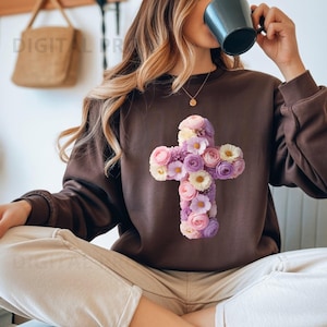 Puede incluir: Una sudadera marrón con un diseño de cruz floral. La cruz está compuesta por flores rosas, moradas y blancas. La sudadera es de color liso y tiene mangas largas. La imagen también muestra a una persona que lleva la sudadera.