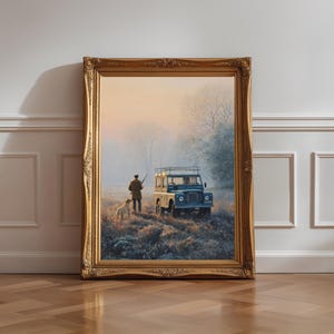 Könnte beinhalten: Ein gerahmtes Wandbild mit einer Landschaftsmalerei, die eine Person mit Hund und einem alten Geländewagen in einem nebligen Feld bei Sonnenaufgang zeigt. Das Kunstwerk befindet sich in einem verzierten, goldfarbenen rechteckigen Rahmen.
