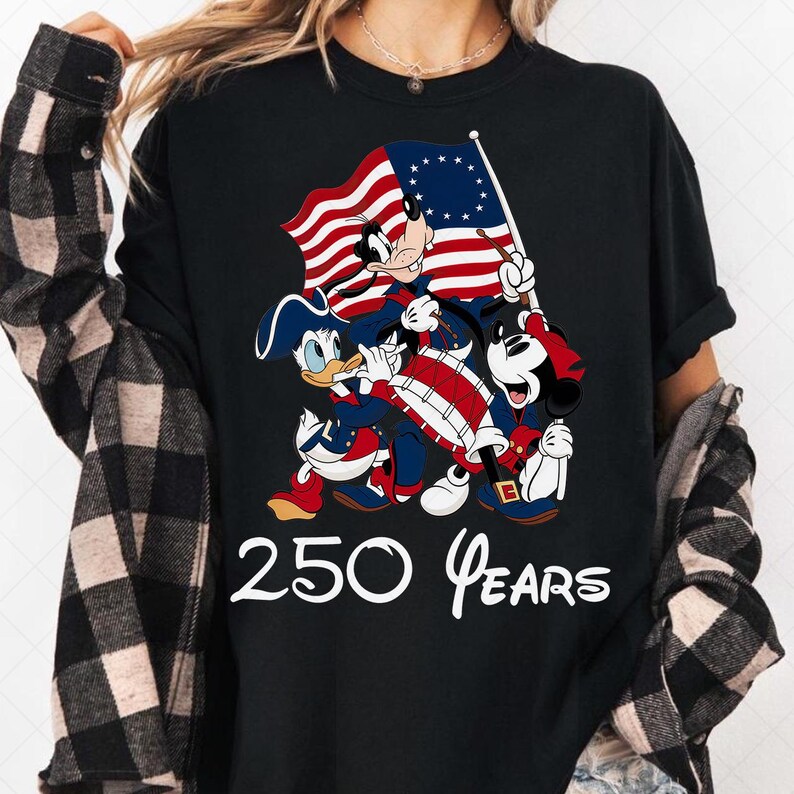 May include: Black t-shirt featuring a patriotic design with cartoon characters. The design includes Mickey Mouse, Donald Duck, and Goofy dressed in colonial attire, holding a flag. The text "250 Years" is displayed in white.