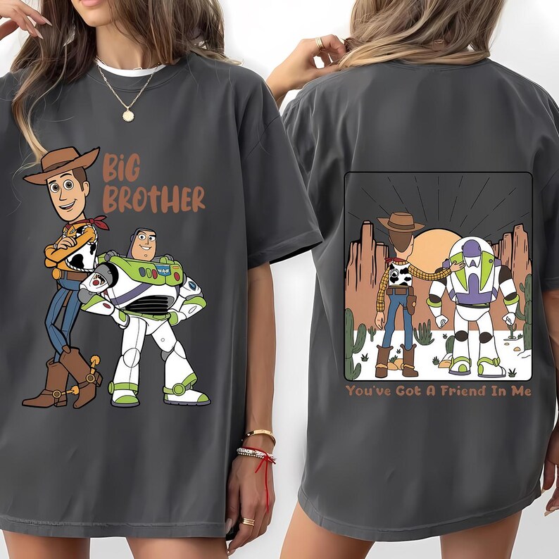 May include: Dark gray t-shirt featuring cartoon characters Woody and Buzz Lightyear. The front of the shirt says "Big Brother". The back of the shirt has a graphic of the characters with the text "You've Got A Friend In Me".