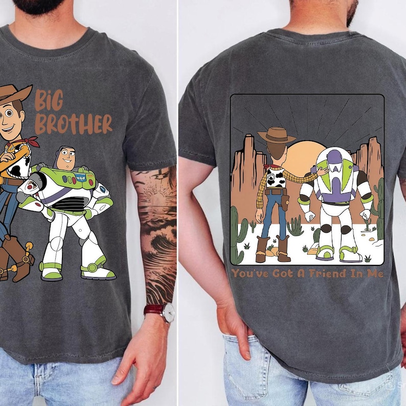 May include: Dark gray t-shirt featuring cartoon characters Woody and Buzz Lightyear. The front of the shirt has the text "Big Brother". The back of the shirt has a desert scene with the text "You've Got A Friend In Me".