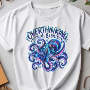 May include: A white t-shirt featuring a colourful graphic of an octopus with blue, purple, and pink hues. The text above the octopus reads "OVERTHINKING ON ALL 8 LEVELS" in a bold, stylised blue font, surrounded by small circular bubbles.