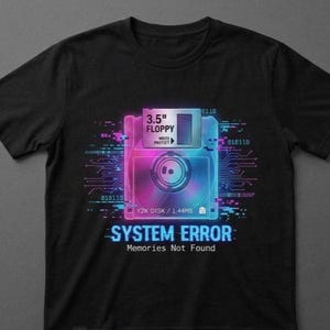 Può includere: T-shirt nera con grafica al neon di un floppy disk da 3,5" e la scritta "SYSTEM ERROR: Memories Not Found". Il design include codice binario e una vivace combinazione di colori blu, viola e rosa.