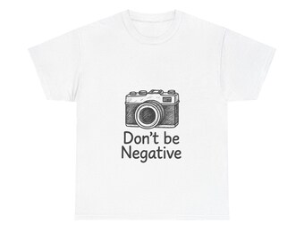 May include: White t-shirt featuring a black and white sketch of a vintage camera. Below the camera is the phrase "Don't be Negative" in black text. The shirt is a casual wear item.