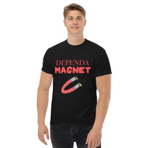 Op de afbeelding: Zwart T-shirt met de tekst "DEPEND A MAGNET" in het rood en een cartoon magneet afbeelding. Het shirt heeft een ronde hals.