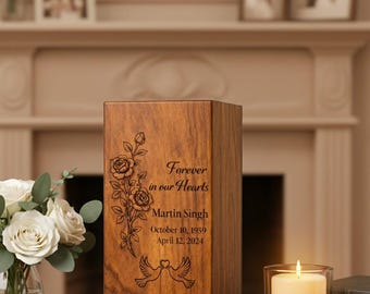 May include: A wooden urn with engraved floral and dove designs. Text reads "Forever in our Hearts," the name "Martin Singh," and dates "October 10, 1959 - April 12, 2024." A lit candle and flowers are in the background.
