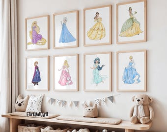 Op de afbeelding: Acht ingelijste aquarelprints van Disney-prinsessen in hun iconische jurken. Het kunstwerk toont Rapunzel, Elsa, Belle, Tiana, Anna, Aurora, Jasmine en Assepoester. De prints worden tentoongesteld boven een houten bank met decoratieve kussens en manden.