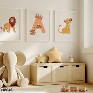 Puede incluir: Tres impresiones artísticas enmarcadas que representan un león, la letra A con una corona y el nombre "Alex", y un cachorro de león. Un elefante de peluche y cojines en forma de estrella están cerca de un mueble de almacenamiento de madera. Un tren de juguete está en el suelo.