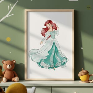 May include: A framed print featuring a watercolor illustration of a princess with long red hair and a flowing teal and white gown. The artwork is displayed in a light wood frame, suitable for a child's room or nursery.