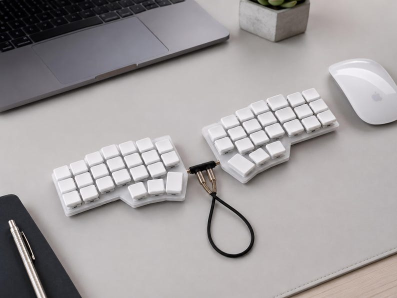 May include: A split ergonomic keyboard featuring two separate white sections with blank white keycaps. The two halves are connected by a short black cable with metallic connectors, creating a distinct layout designed for two-handed typing.