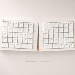 May include: A white split keyboard with a curved design. The keys are white with black lettering. The keyboard is divided into two sections, with the text "Endless Fun, One Keyboard" below.
