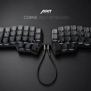 Può includere: Una tastiera divisa Corne nera con tasti scuri. La tastiera è collegata da un cavo nero. Il testo "ART" e "CORNE SPLIT KEYBOARD" sono visualizzati in bianco.