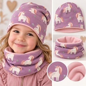 Peut inclure: Un ensemble bonnet et tour de cou violet orné d'un motif répétitif de licornes blanches aux crinières et queues roses. Les deux pièces sont doublées d'un tissu rose clair uni et doux, avec une petite étiquette blanche portant un cœur.