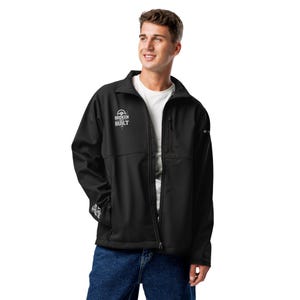 May include: Black softshell jacket with the text "BROKEN BUILT" in white on the chest. The jacket has a zip-up front, a small chest pocket, and a collar. The person in the image is wearing blue jeans and a white t-shirt.