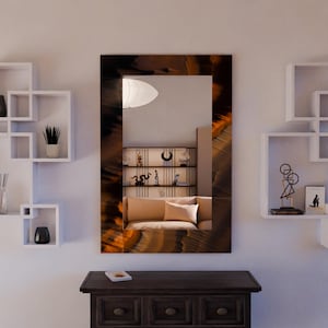 May include: A rectangular wall mirror with a brown and orange patterned frame. The mirror reflects a room with a sofa, shelves, and decorative objects. The mirror is mounted above a dark wooden cabinet.