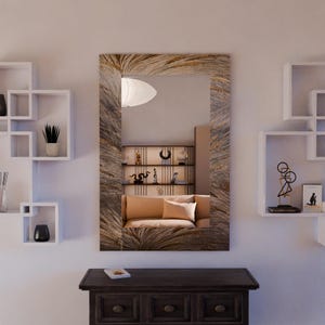 May include: A rectangular mirror with a textured, light brown frame hangs above a dark brown wooden cabinet. The mirror reflects a room with a tan sofa and decorative shelves. White square shelves are on either side.